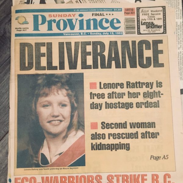 Front page of a yellowing newspaper, the Sunday Province, shows full-page coverage of Lenore's ordeal. The headline reads in large, black all-caps: Deliverance. A graduation photo of a smiling Lenore is next to text that reads "Lenore Rattray is free after her eight-day hostage ordeal; Second woman also rescued after kidnapping". A secondary headline at the bottom of the page in orange reads "Eco-warriors strike B.C."